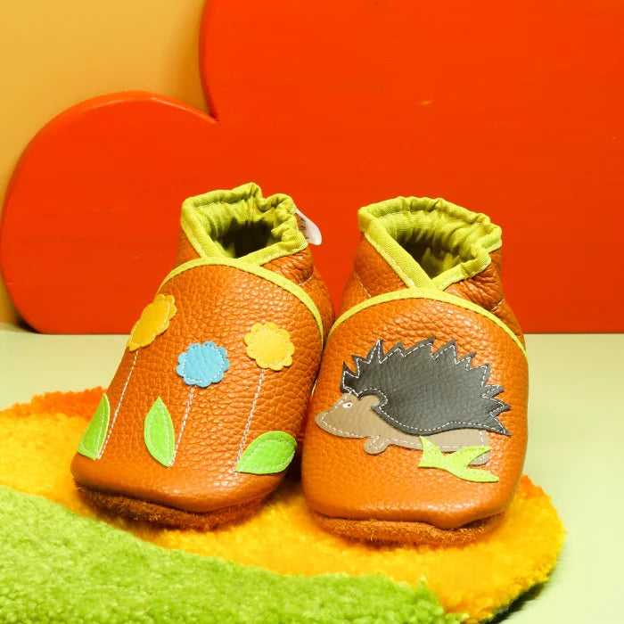 Chaussons bébé en cuir souple orange avec motif hérisson et fleurs colorées, fabrication artisanale.