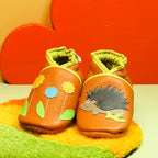 Chaussons bébé en cuir souple orange avec motif hérisson et fleurs colorées, fabrication artisanale.