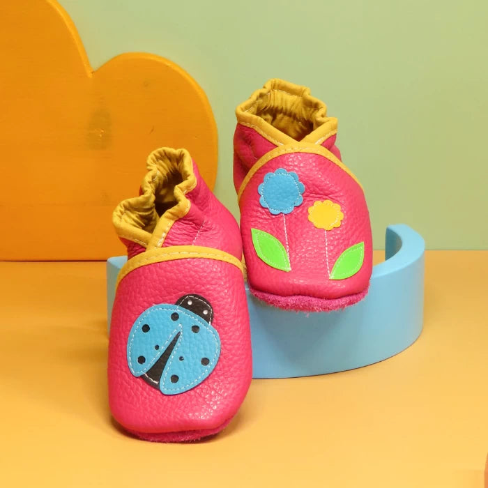 Chaussons bébé en cuir souple rose motif coccinelle et fleurs, vue de face avec finitions jaune moutarde.