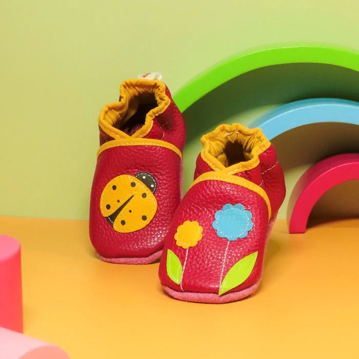 Chaussons bébé en cuir souple rose avec coccinelle et fleurs, vue en hauteur montrant les détails des appliqués.