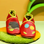 Chaussons en cuir souple rouge pour bébé avec hérisson appliqué et fleurs décoratives sur le dessus.