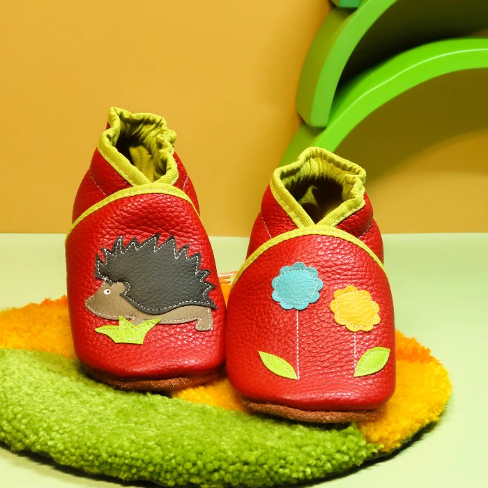 Chaussons en cuir souple rouge pour bébé avec hérisson appliqué et fleurs décoratives sur le dessus.