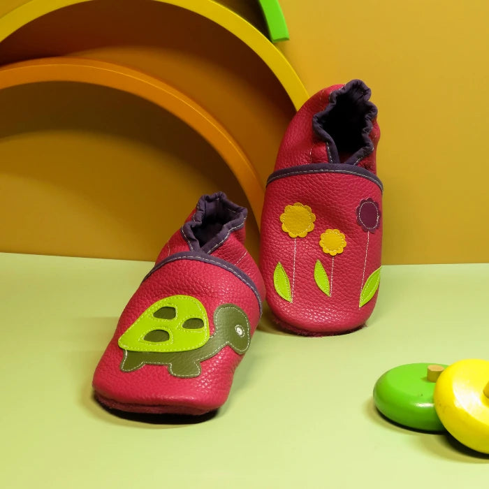 Chaussons bébé en cuir souple rouge avec tortue verte et fleurs jaunes et violettes, fabrication artisanale.