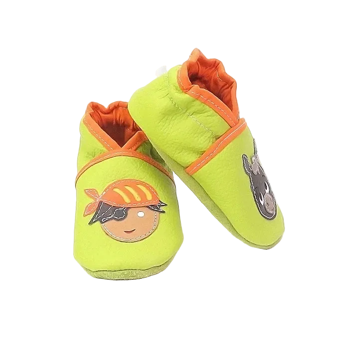 Chaussons bébé en cuir souple vert anis motif pirate et âne, vue en biais mettant en valeur les appliqués et les finitions orange.