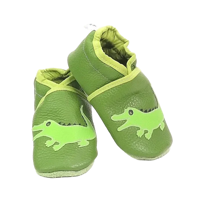 Chaussons bébé en cuir souple vert motif crocodile, vue en biais montrant les détails de l’appliqué et la texture du cuir.