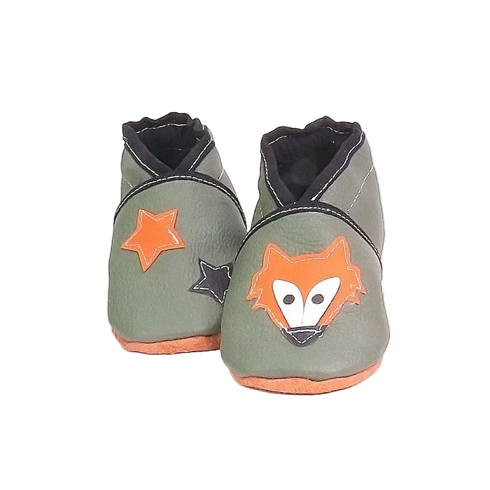 Chaussons en cuir souple artisanaux vert kaki pour bébé avec tête de renard orange sur un pied et étoiles orange et noire sur l’autre.