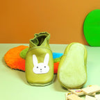 Chaussons en cuir souple vert pour bébé avec tête de lapin blanche, vue montrant le motif et la semelle en cuir retourné.