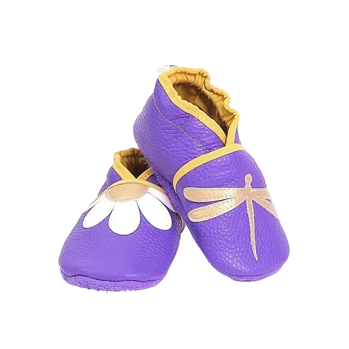 Chaussons bébé en cuir souple violet motif libellule et marguerite, vue en biais mettant en valeur les appliqués et les finitions jaune moutarde.