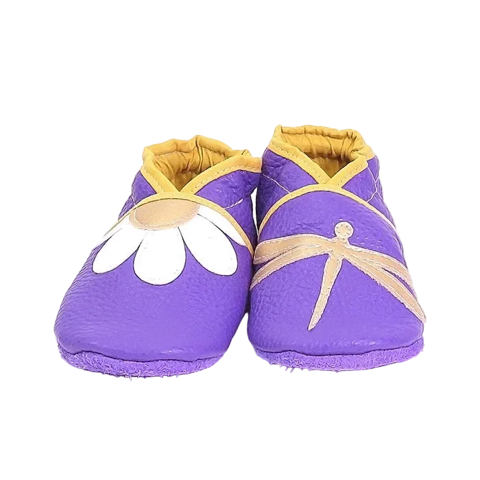 Chaussons en cuir souple artisanaux violet pour bébé avec marguerite blanche sur un pied et libellule beige sur l’autre, finitions jaune moutarde.