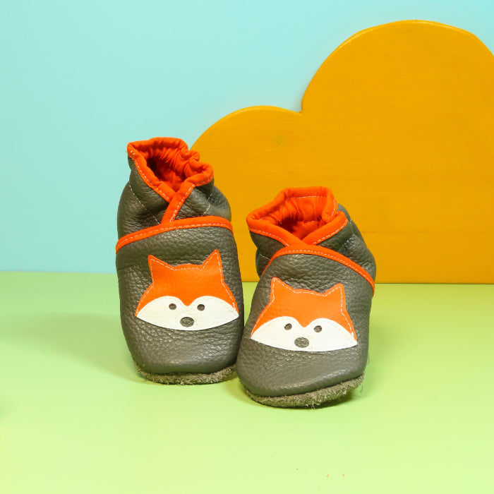 Chaussons en cuir souple artisanaux gris pour enfant avec tête de renard orange et finitions orange.