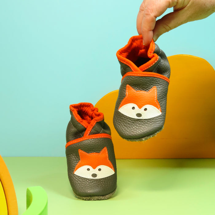 Chaussons en cuir souple artisanaux gris pour enfant avec motif renard orange, chausson tenu en main montrant la souplesse.