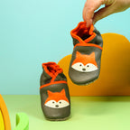 Chaussons en cuir souple artisanaux gris pour enfant avec motif renard orange, chausson tenu en main montrant la souplesse.