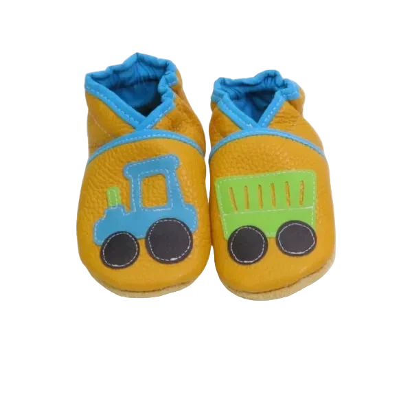 Chaussons en cuir souple artisanaux jaunes pour enfant avec tracteur bleu sur un pied et remorque verte sur l’autre, finitions bleues.