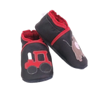 Chaussons en cuir souple artisanaux noirs pour enfant, vue en angle, avec tracteur rouge sur un pied et petit taureau marron sur l’autre, finitions rouges.
