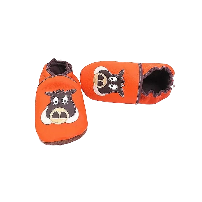Chaussons en cuir souple artisanaux orange pour enfant avec motif sanglier, vue inclinée avec un chausson allongé.