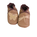Chaussons en cuir souple artisanaux couleur cappucino pour enfant, avec papillon beige sur un pied et libellule beige sur l’autre, finitions marron.