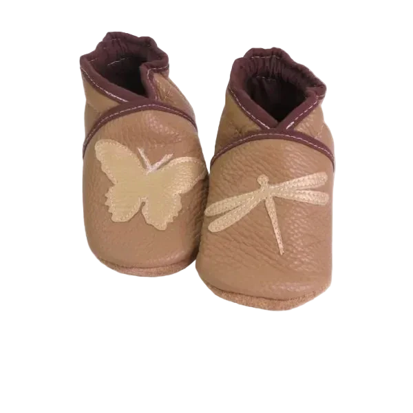 Chaussons en cuir souple artisanaux couleur cappucino pour enfant, avec papillon beige sur un pied et libellule beige sur l’autre, finitions marron.