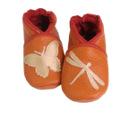 Chaussons en cuir souple artisanaux orange pour enfant, avec papillon crème sur un pied et libellule crème sur l’autre, finition élastiquée .